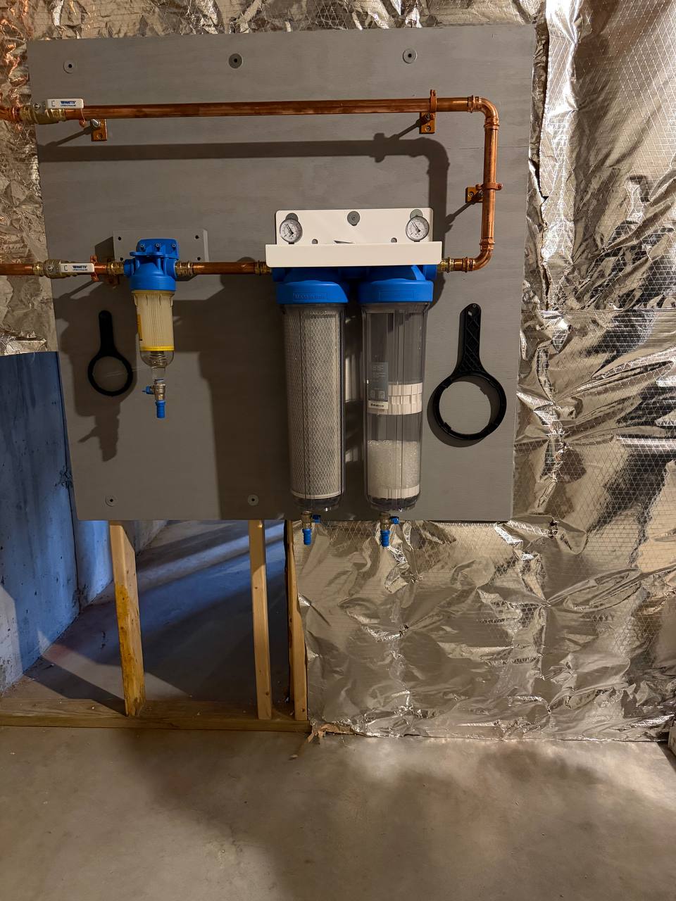 Whole-house water filtration housings and copper piping mounted on a board in a basement