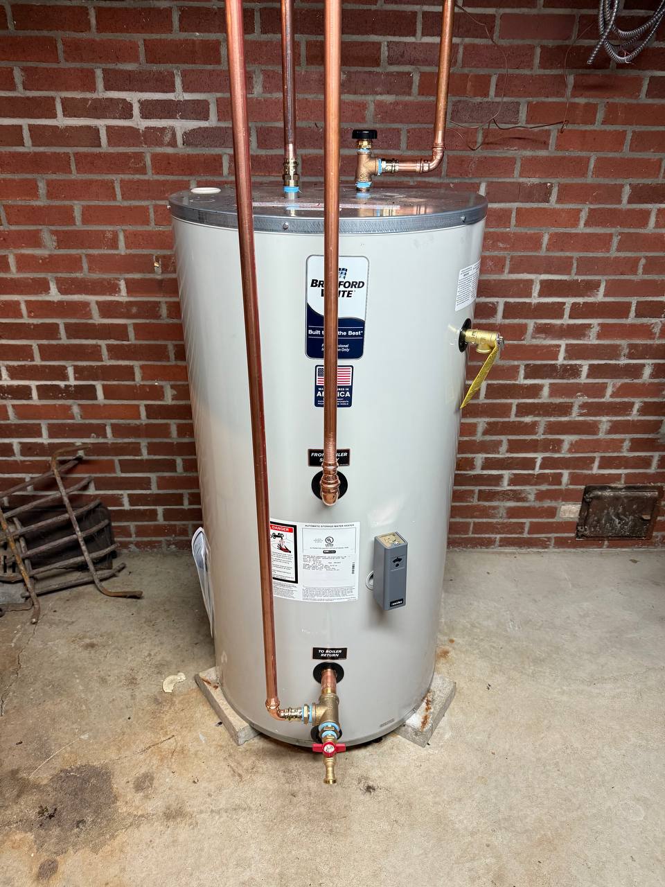 Indirect water heater with copper riser pipes and shut-off valves against a brick wall