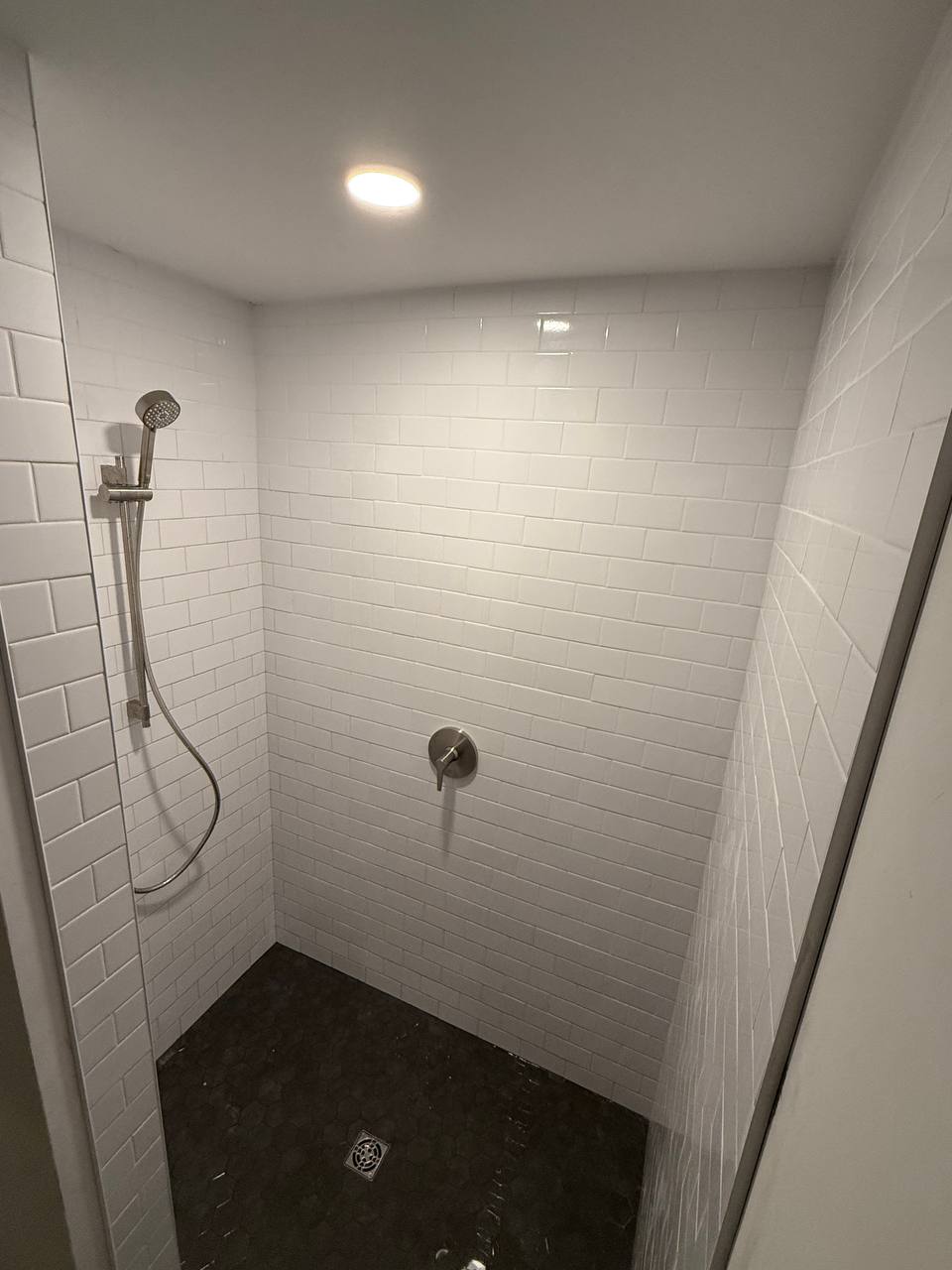Tiled walk-in shower with handheld sprayer on slide bar and hex mosaic floor