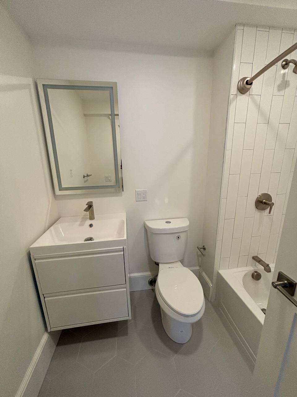 Bathroom with wall-mounted vanity, toilet and tiled tub-shower with lighted mirror