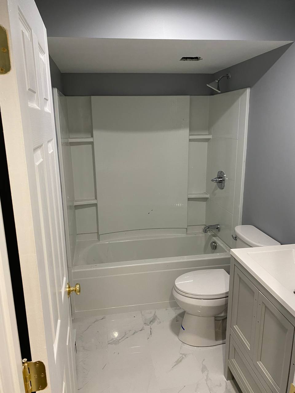 Bathroom with alcove tub and shower surround, toilet and vanity on marble-look tile
