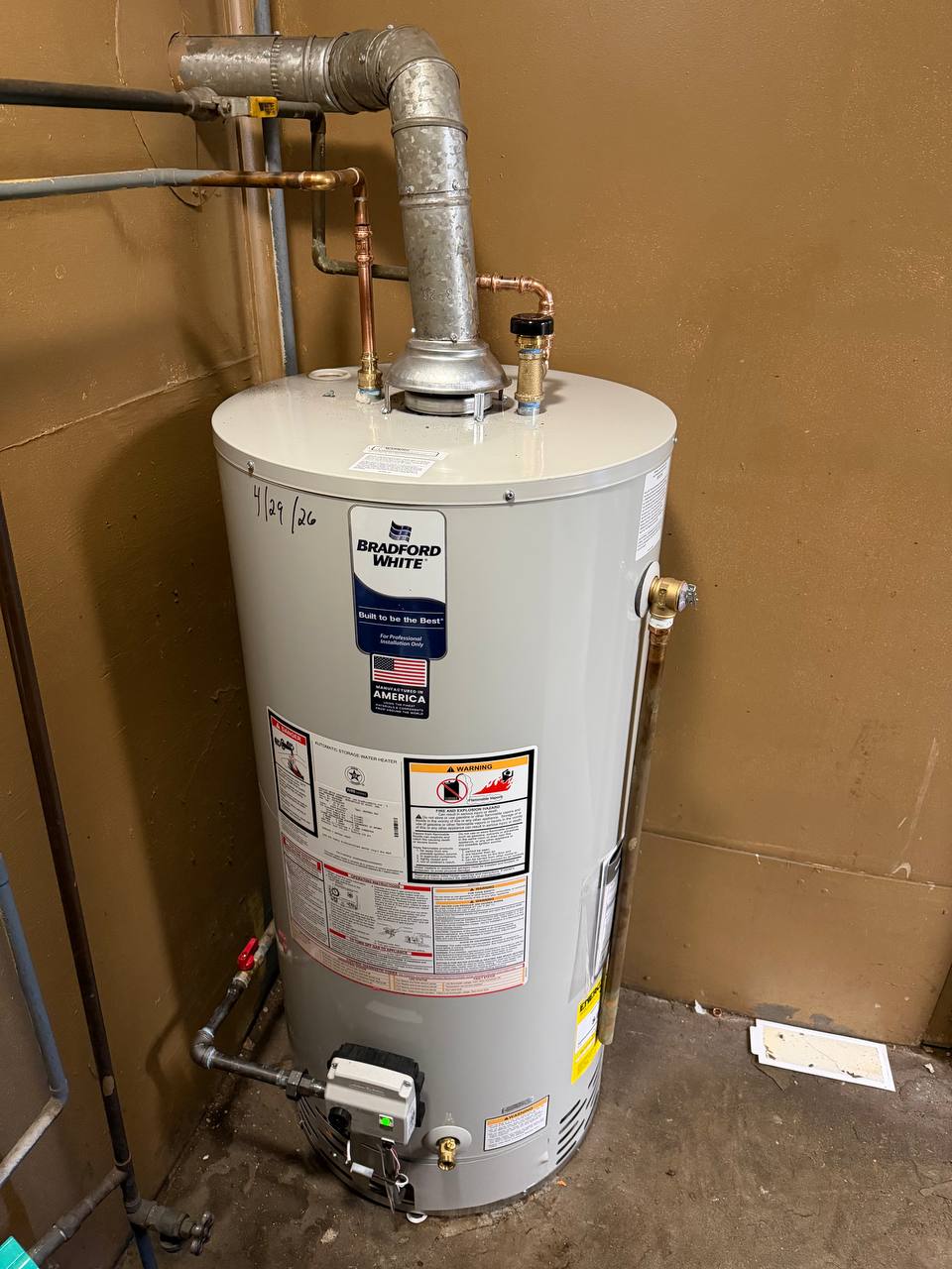 Gas water heater with galvanized flue vent and copper supply lines against a wall